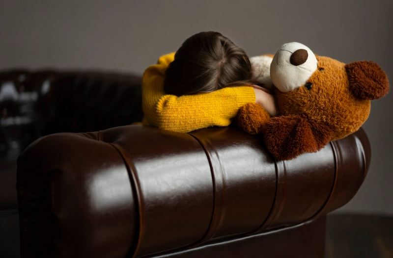 distressed child hiding behind teddy bear