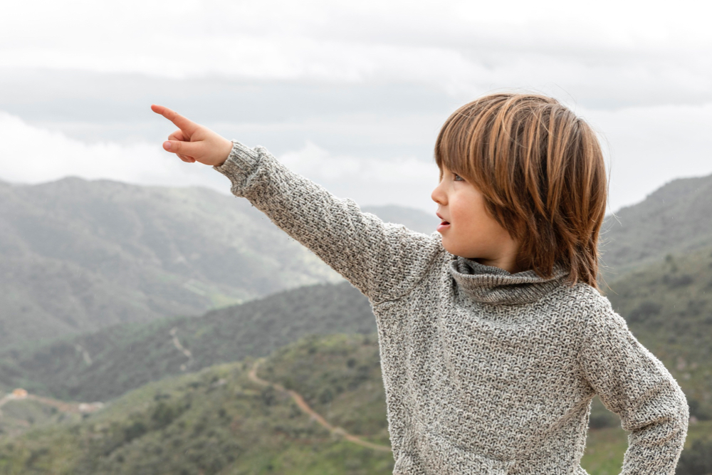 boy in the mountains pointing up at the sky