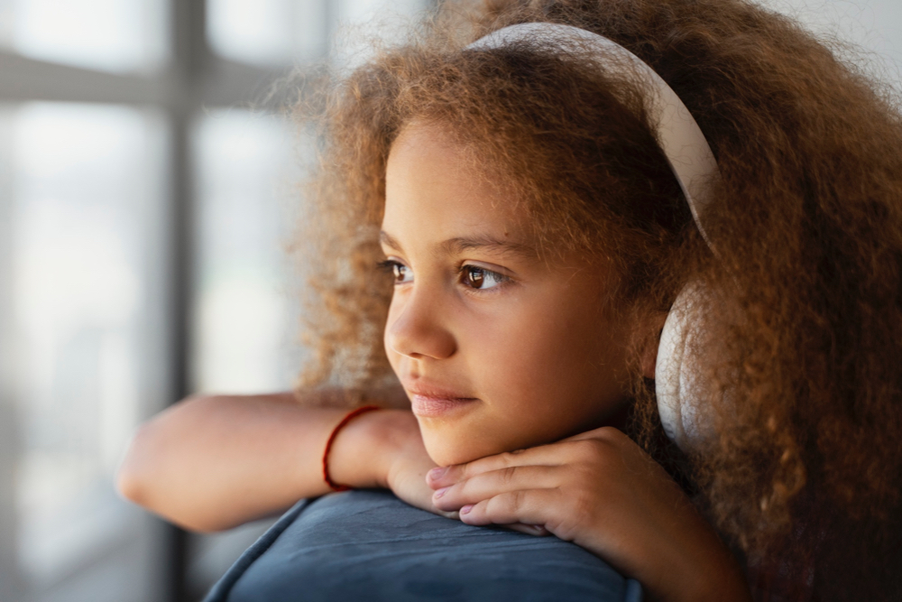 young girl with headphones on looking out the window