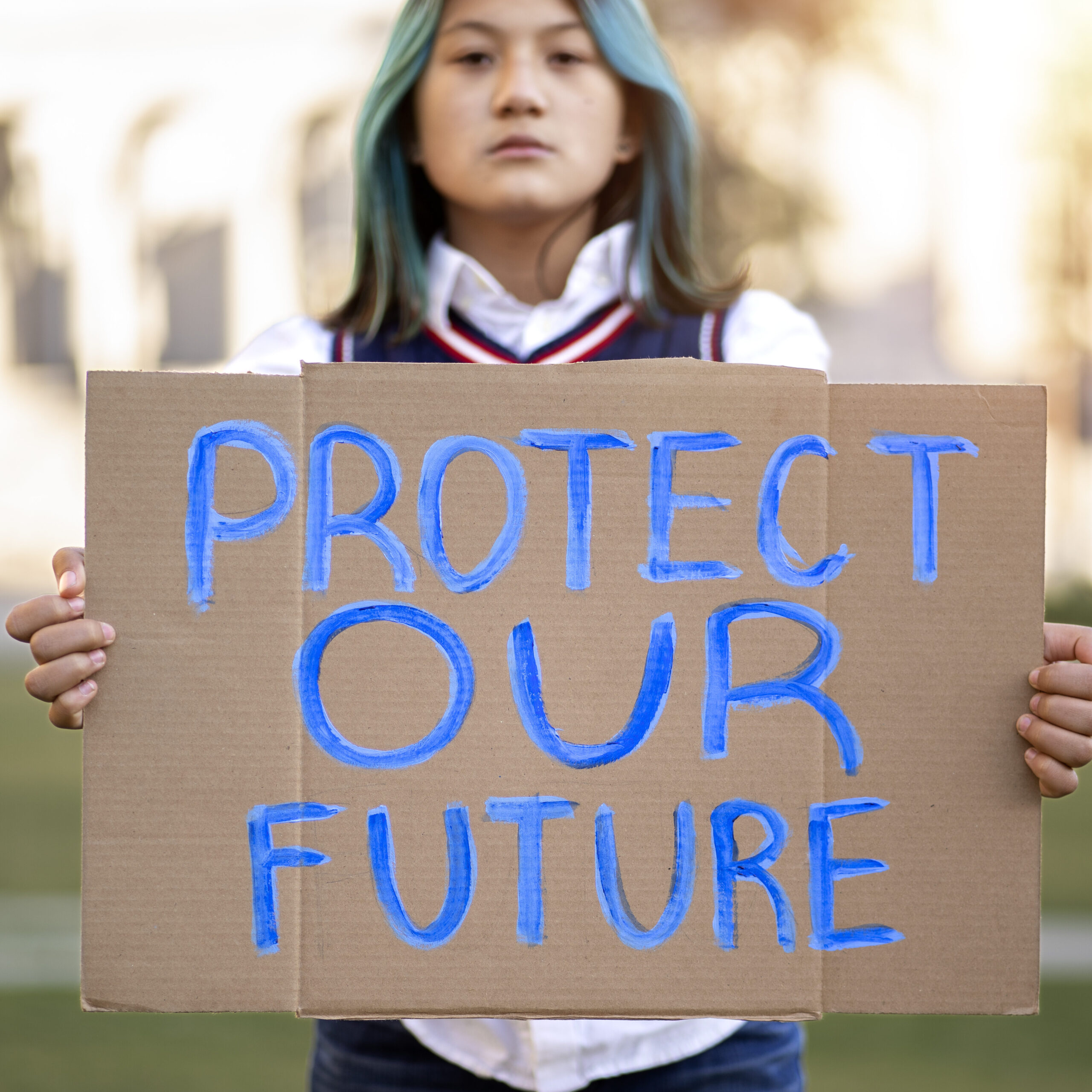 Young person protesting, placard reads: Protect Our Future.