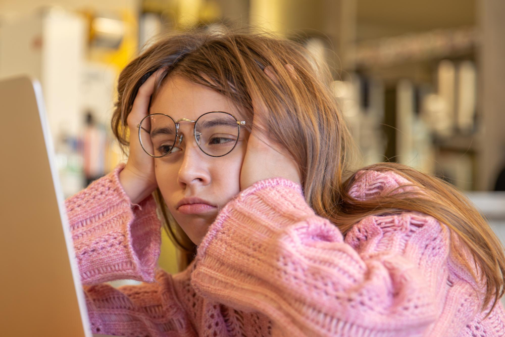Girl wit glasses looking bored at her laptop.